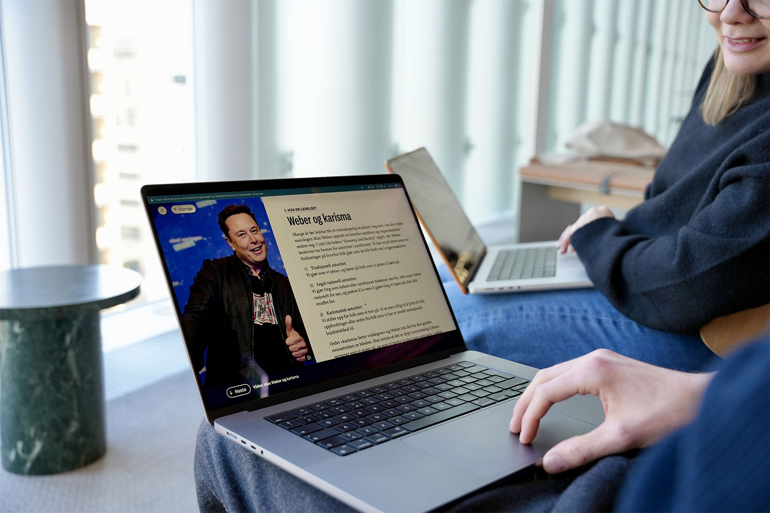 Bildet viser en PC-skjerm av Kunne Organisasjon og ledelse. På PC-skjermen kan man se et bilde av Elon Musk og deler at teksten fra kapittelet om Weber og karisma.