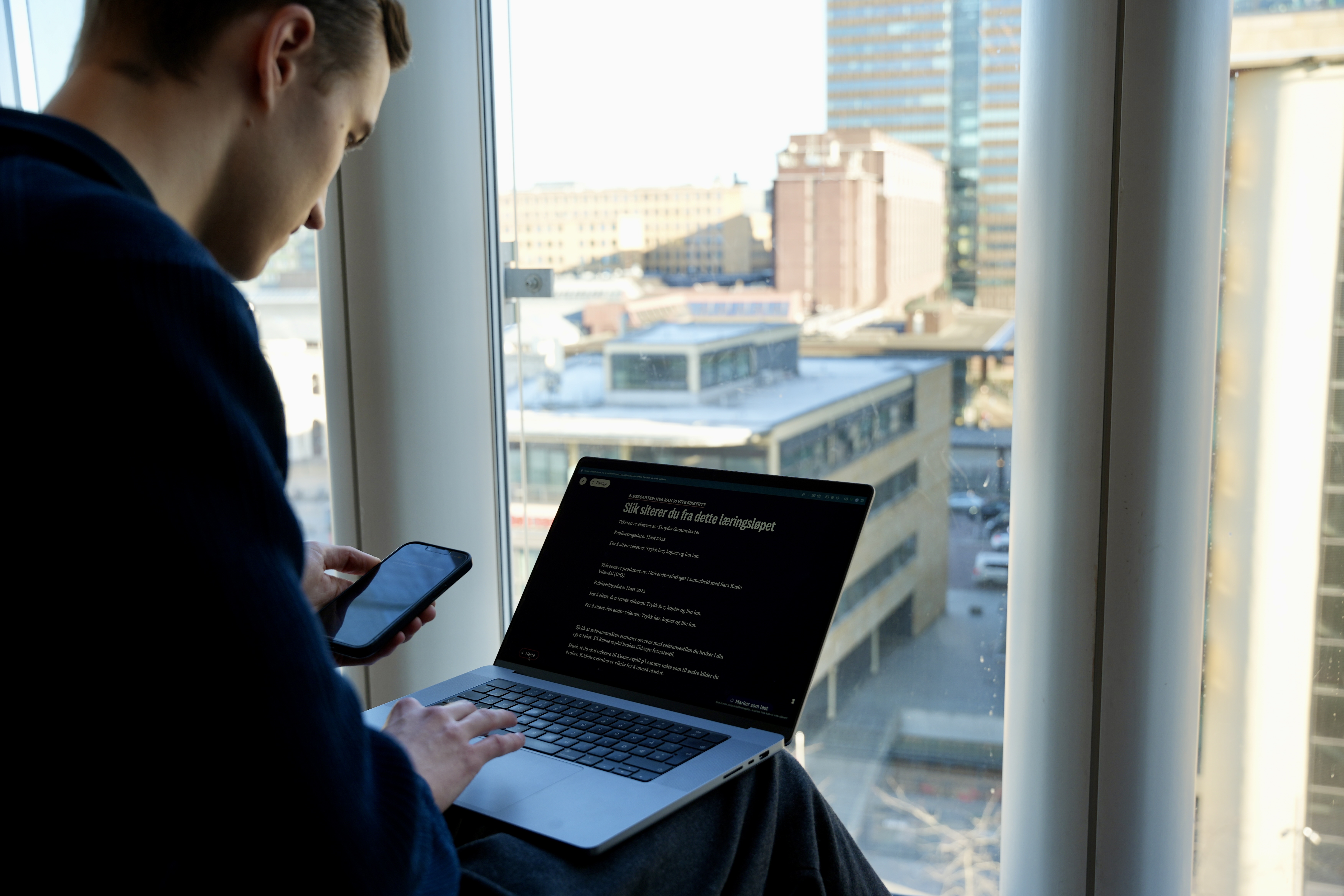 Bildet viser en student som ser på pc-skjermen samtidig som han holder en mobiltelefon i hånden.