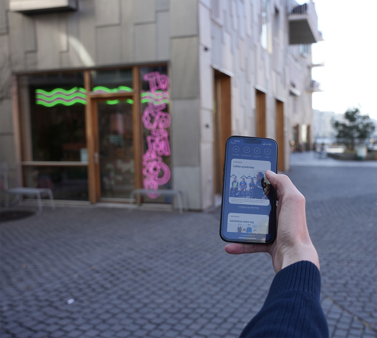 Student som bruker Kunne på en mobilen på vei til lesesalen mens hen drikker en kopp kaffe.